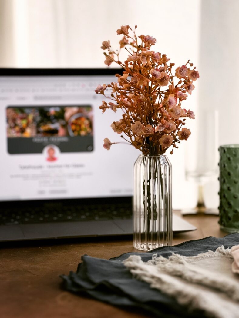 Laptop mit einer Vase mit Blumen im Vordergrund